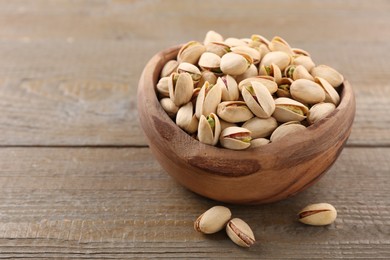 Photo of Delicious pistachios in bowl on wooden table. Space for text