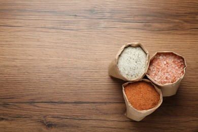 Photo of Different kinds of salt in paper bags on wooden table, flat lay. Space for text