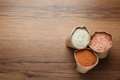 Different kinds of salt in paper bags on wooden table, flat lay. Space for text