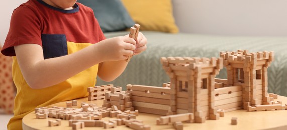 Photo of Little boy playing with wooden construction set at table indoors, closeup. Child's toy