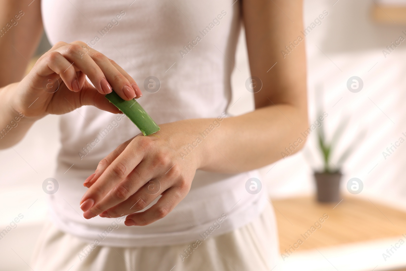 Photo of Young woman applying aloe gel from leaf onto her hand in bathroom, closeup