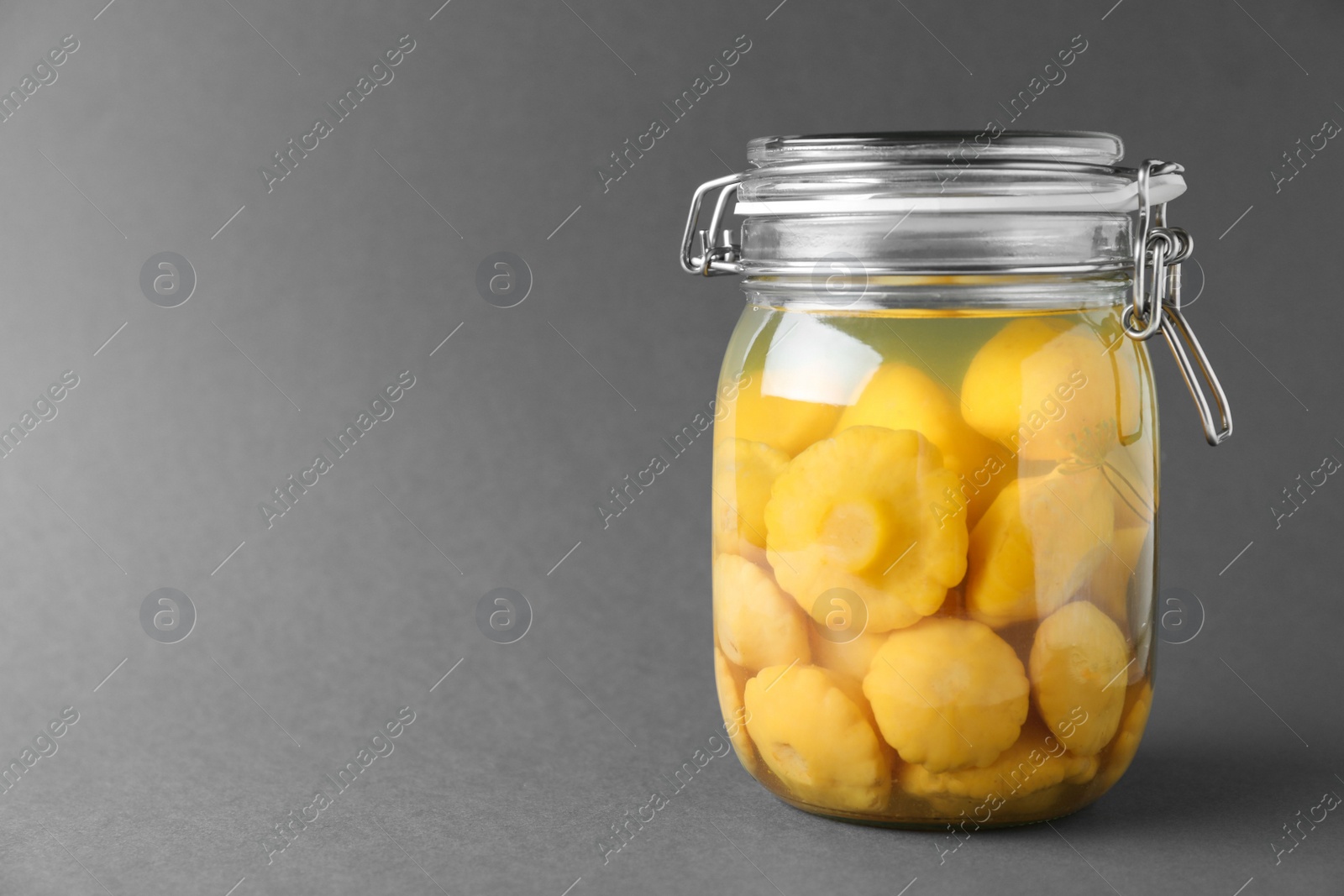 Photo of Jar of pickled custard squashes on grey background. Space for text