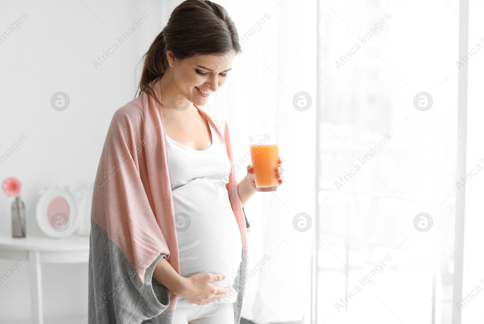 Photo of Young pregnant woman holding glass with juice at home