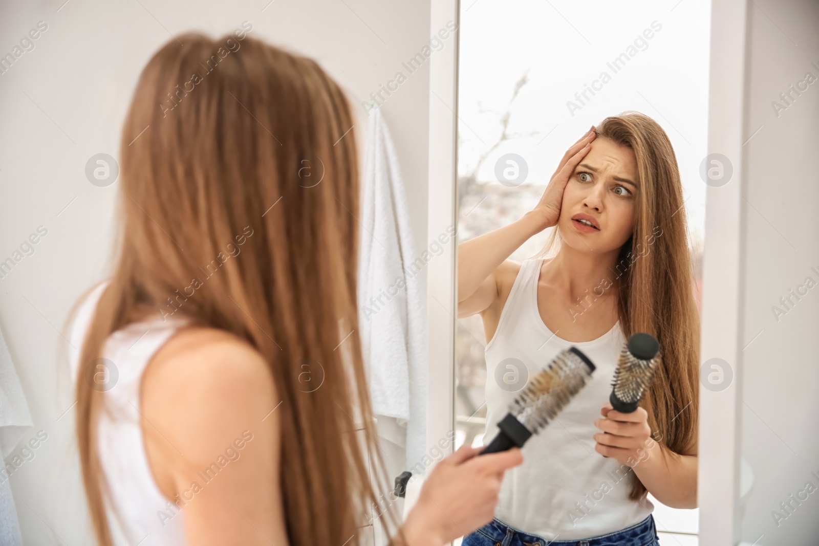 Photo of Young woman with hair loss problem looking in mirror indoors