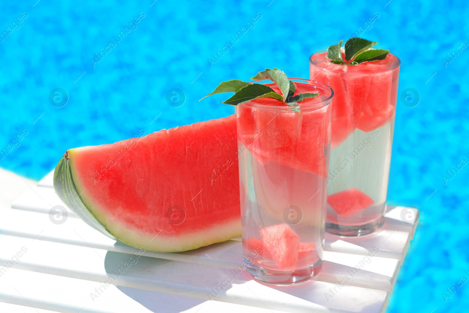 Photo of Refreshing drink in glasses and sliced watermelon near swimming pool outdoors