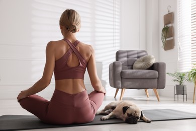 Woman with dog practicing yoga at home, back view