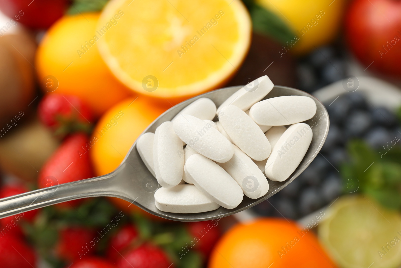 Photo of Vitamin pills in spoon over fresh fruits, closeup