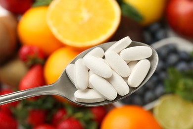 Photo of Vitamin pills in spoon over fresh fruits, closeup