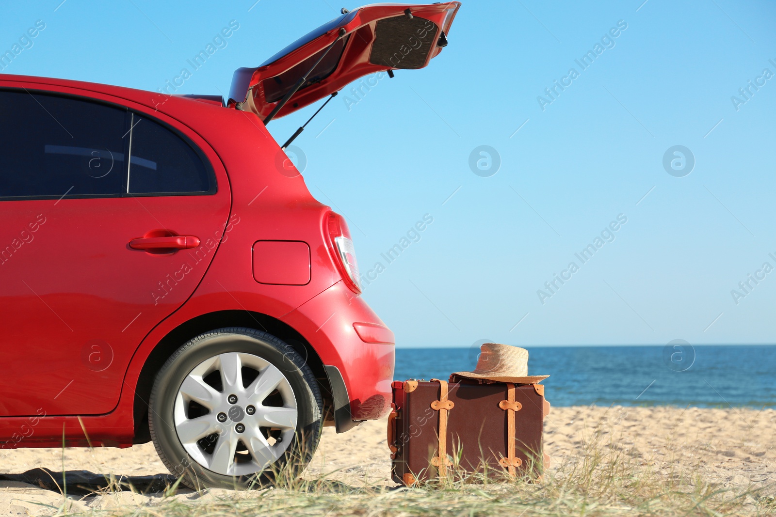 Photo of Modern car, retro suitcase and hat on sand near sea, space for text. Beach accessories