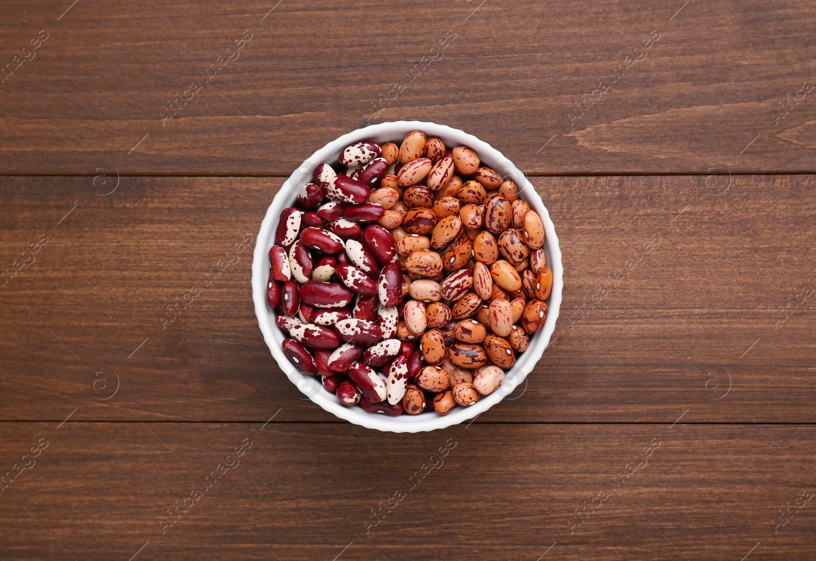 Photo of Different kinds of dry kidney beans in bowl on wooden table, top view