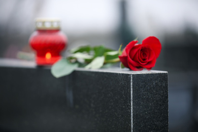 Photo of Red rose and candle on black granite tombstone outdoors. Funeral ceremony