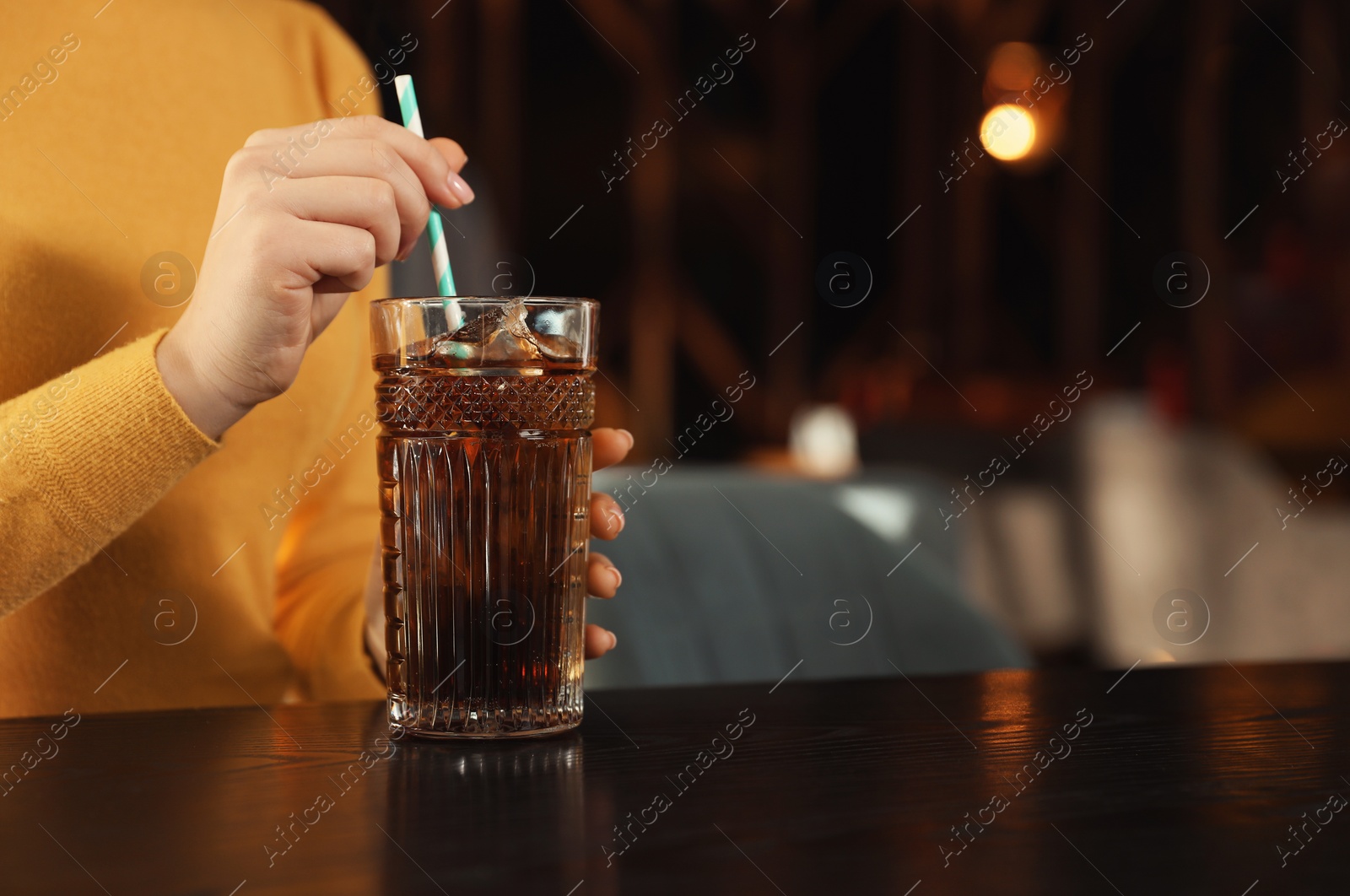 Photo of Woman with glass of refreshing cola at table indoors, closeup. Space for text