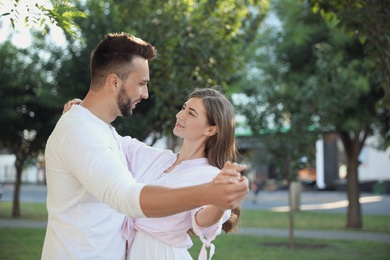 Lovely young couple dancing together in park on sunny day