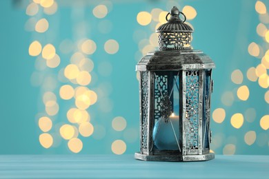 Photo of Traditional Arabic lantern on table against light blue background with blurred lights. Space for text