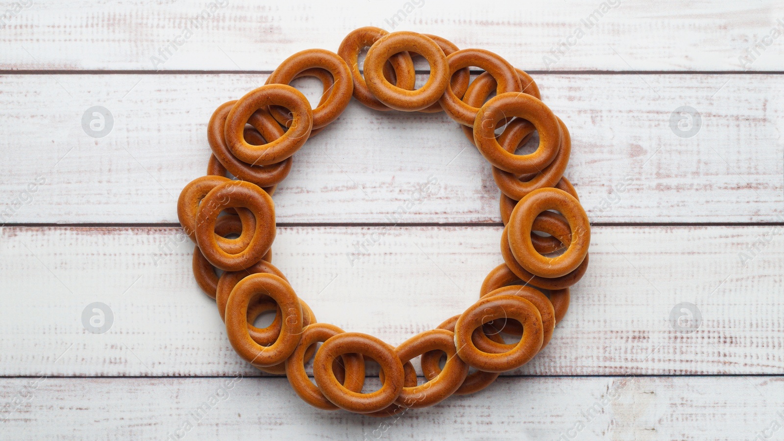 Photo of Frame made of tasty dry bagels (sushki) on white wooden table, flat lay. Space for text