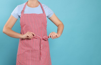 Photo of Woman in clean striped apron on light blue background, closeup. Space for text