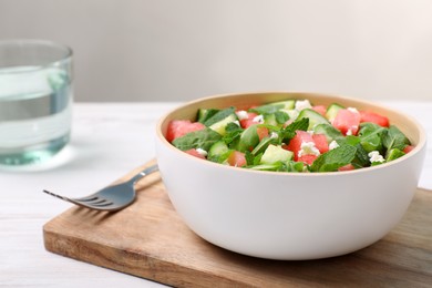 Photo of Delicious salad with watermelon, cucumber, arugula and feta cheese served on white wooden table