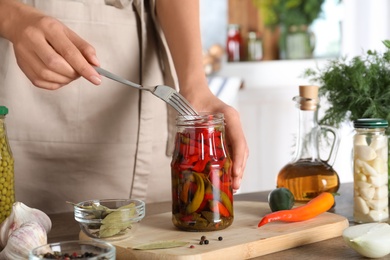 Photo of Woman taking pickled chili pepper from jar at wooden table indoors, closeup