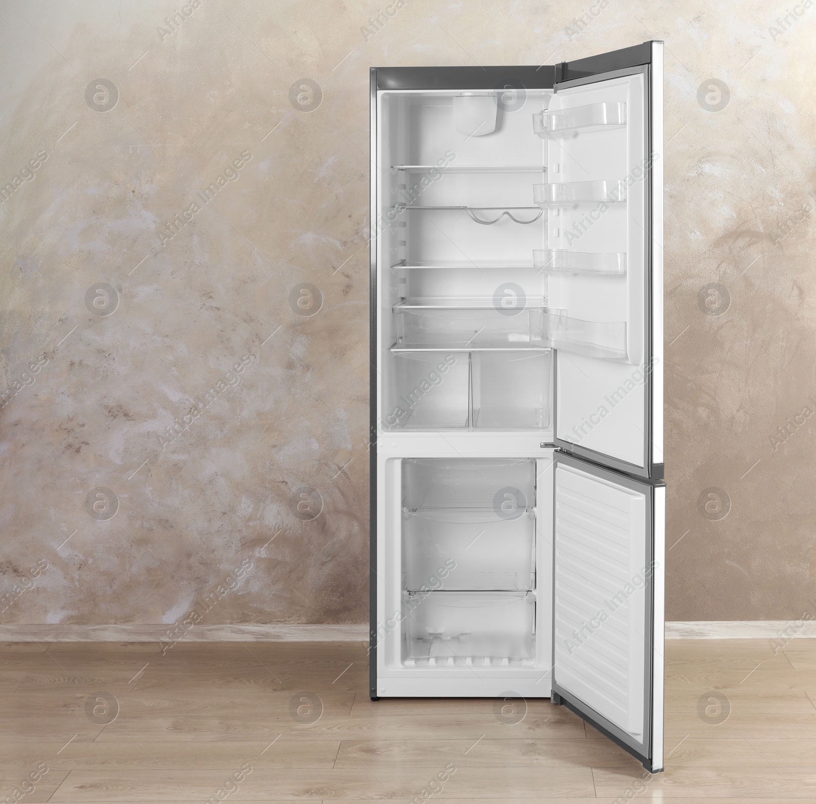 Photo of Open refrigerator with empty shelves near grey wall indoors. Space for text