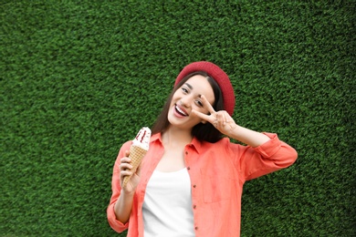 Photo of Happy young woman with delicious ice cream in waffle cone near grass wall