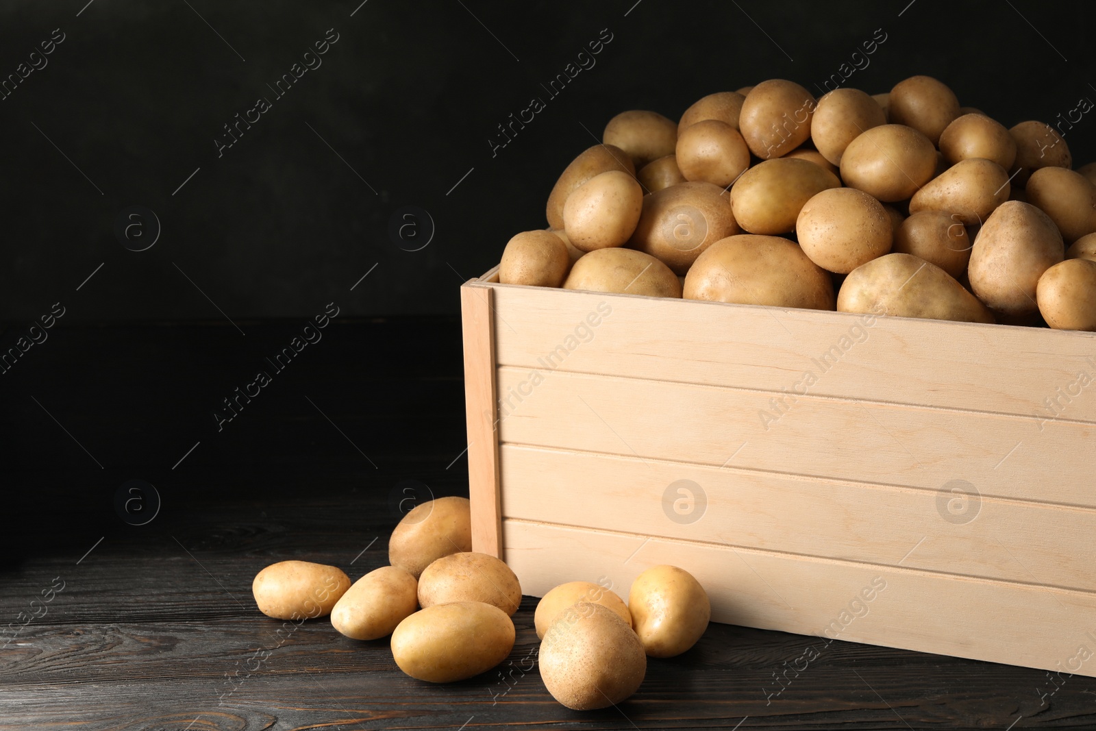 Photo of Raw fresh organic potatoes on wooden table against dark background. Space for text