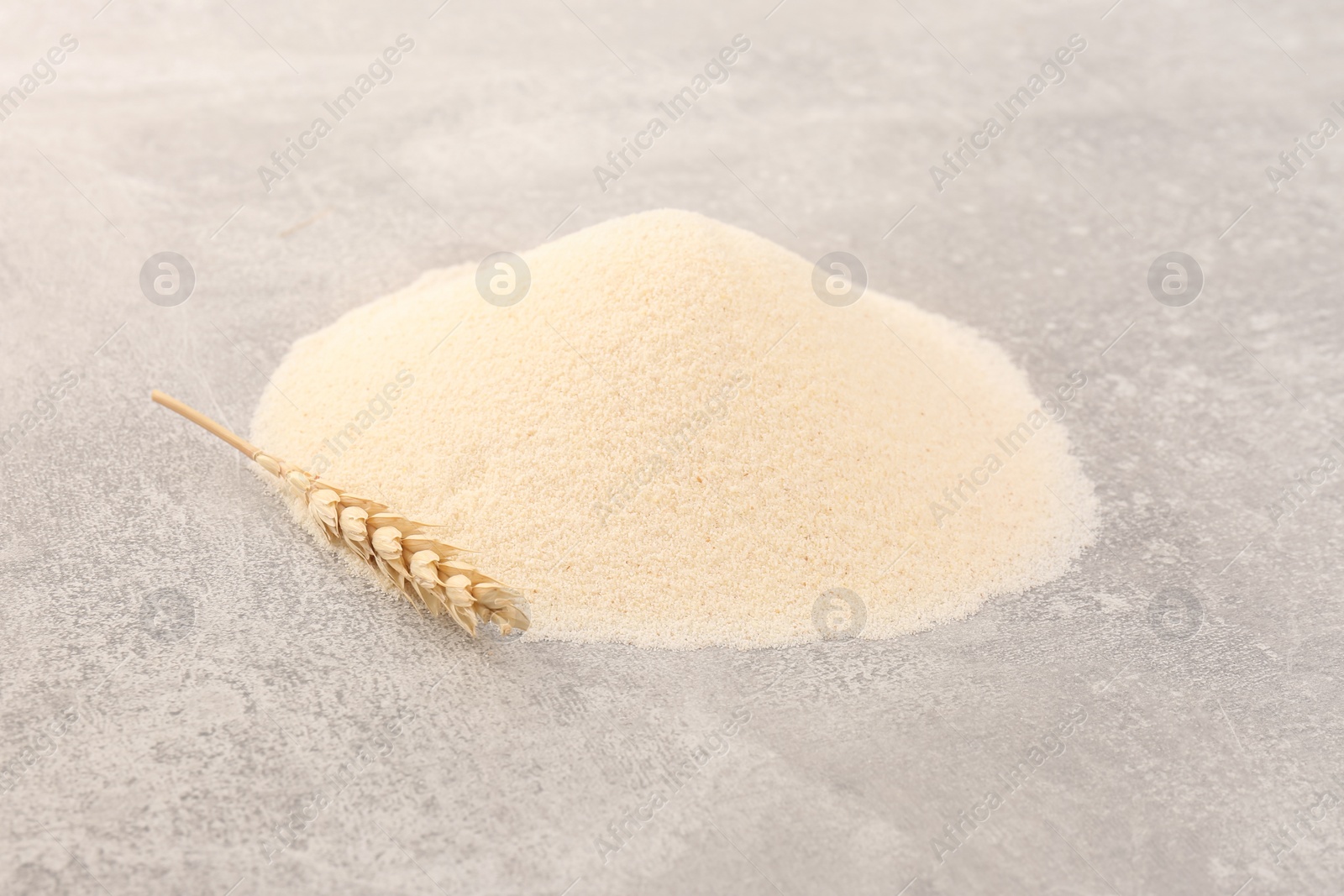 Photo of Pile of uncooked organic semolina and spikelet on grey table