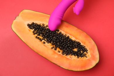 Half of papaya and purple vibrator on red background, top view. Sex concept