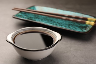 Photo of Bowl of soy sauce and chopsticks on grey table, closeup