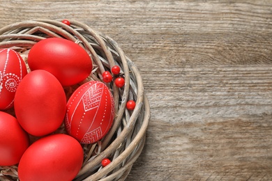 Photo of Wicker nest with painted Easter eggs on wooden table, above view. Space for text