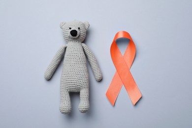 Orange ribbon and toy bear on light grey background, flat lay. Multiple sclerosis awareness