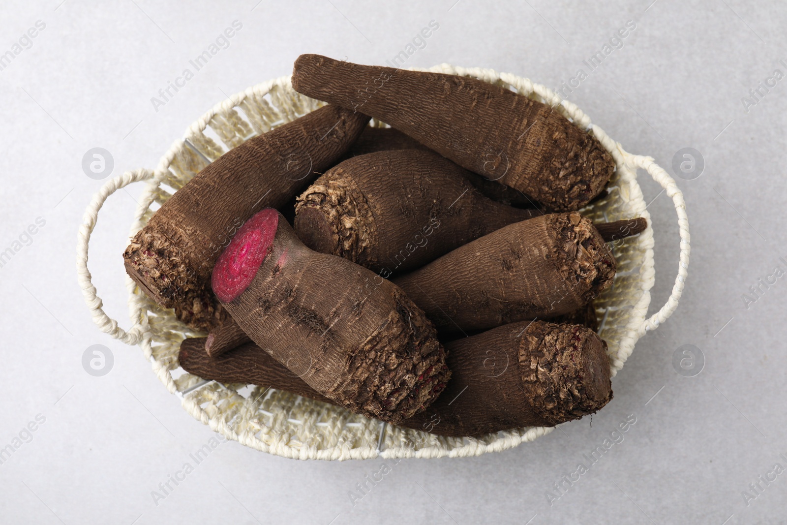 Photo of Whole and cut red beets in basket on light gray table, top view