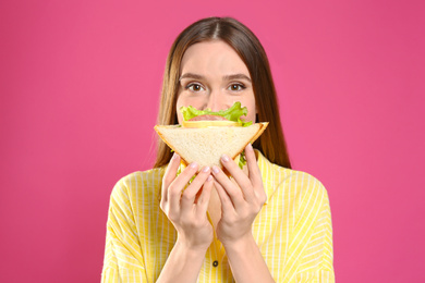 Young woman eating tasty sandwich on pink background