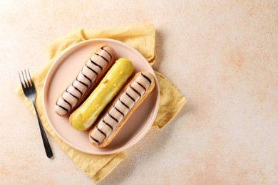 Photo of Different tasty glazed eclairs served on color textured table, top view. Space for text