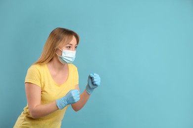 Photo of Woman with protective mask and gloves in fighting pose on light blue background, space for text. Strong immunity concept