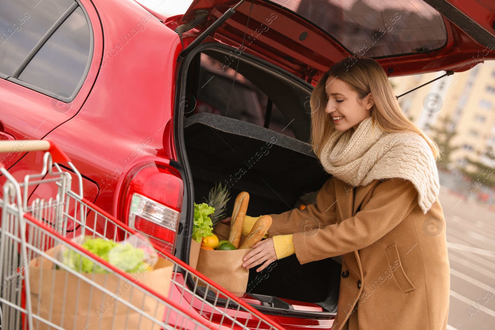 Photo of Young woman putting bag of groceries into her car outdoors