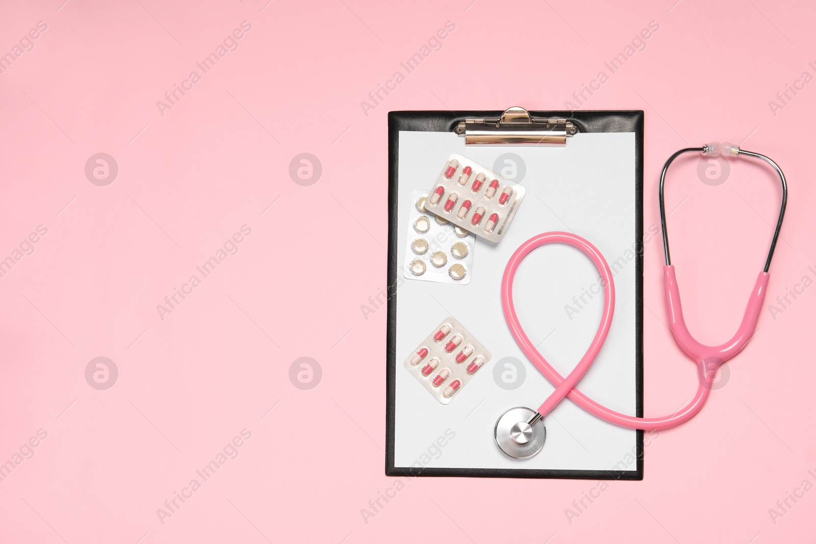 Photo of Stethoscope, clipboard and pills on pink background, top view. Space for text