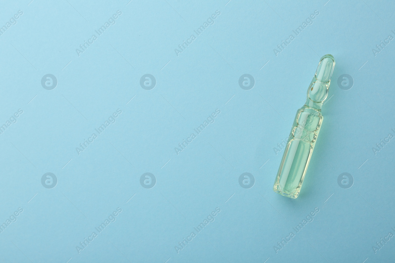 Photo of Glass ampoule with liquid on light blue background, top view. Space for text