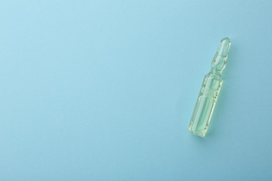 Photo of Glass ampoule with liquid on light blue background, top view. Space for text