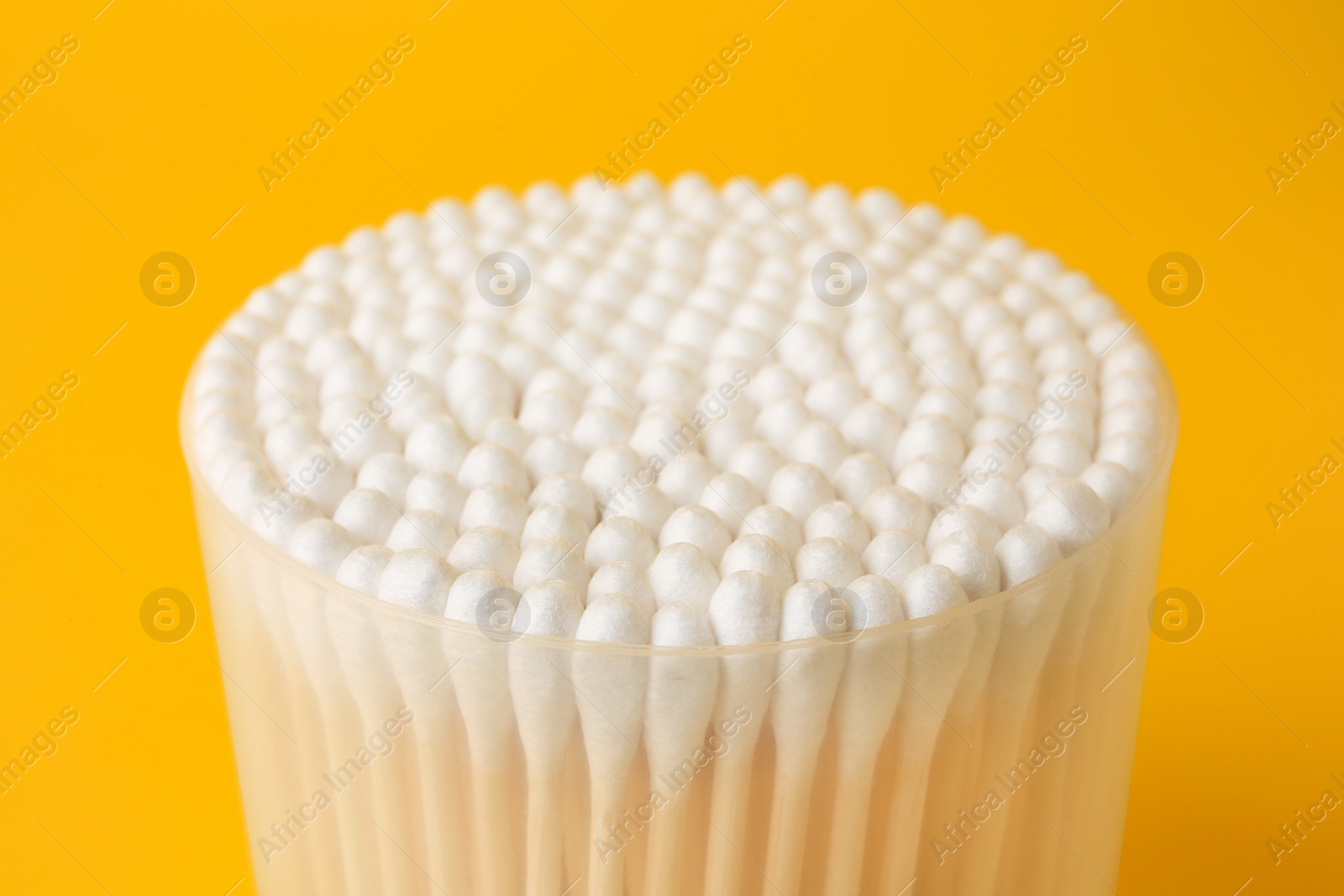 Photo of Container with new cotton buds on yellow background, closeup