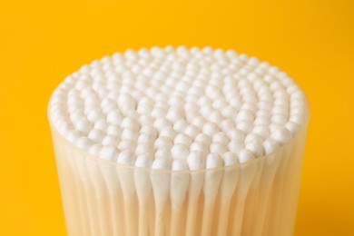 Container with new cotton buds on yellow background, closeup