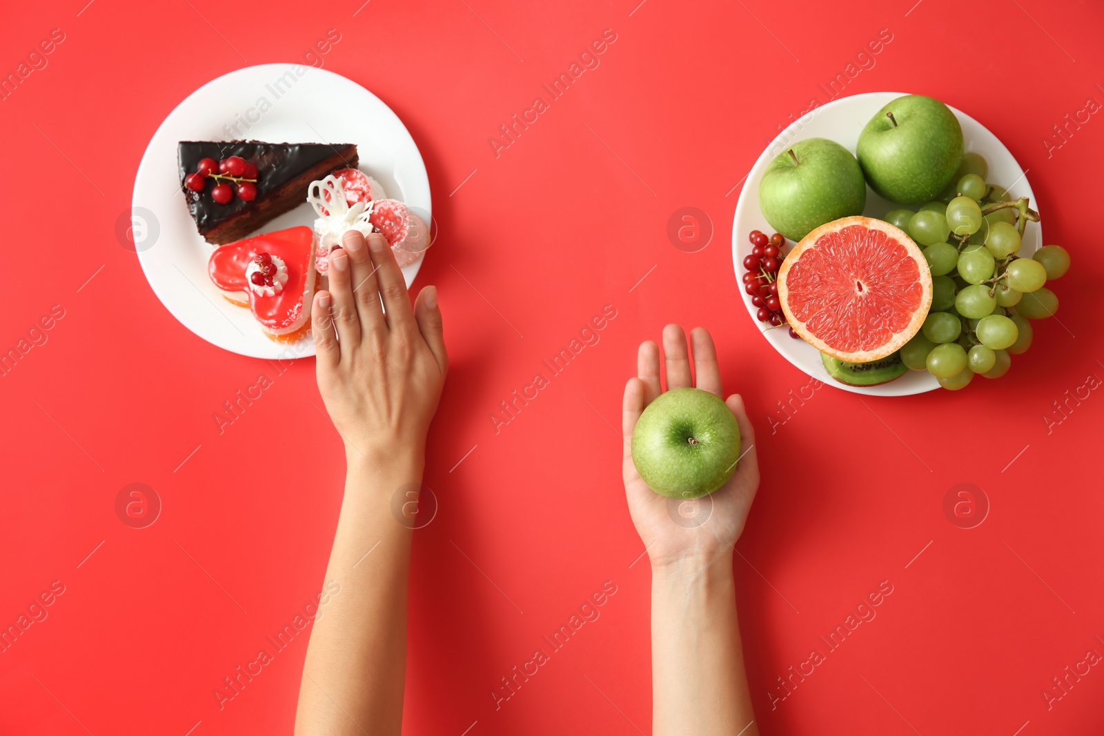 Photo of Top view of woman choosing between sweets and healthy fruits on red background, closeup