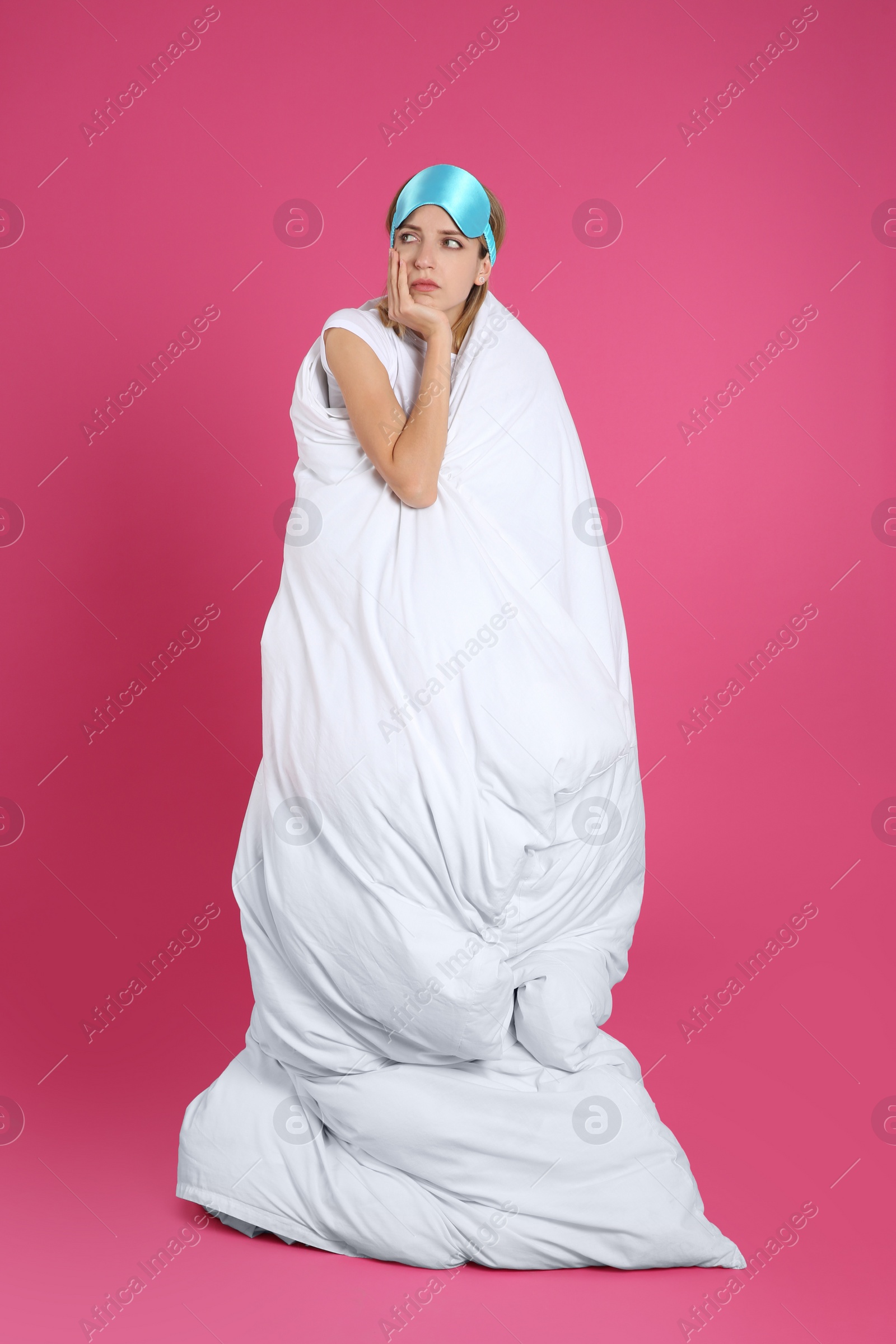 Photo of Young woman in sleeping mask wrapped with soft blanket on pink background