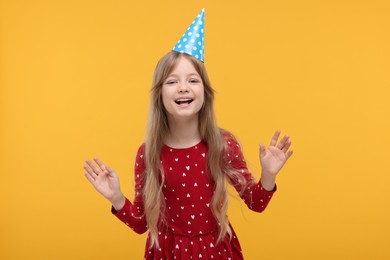 Happy little girl in party hat dancing on yellow background