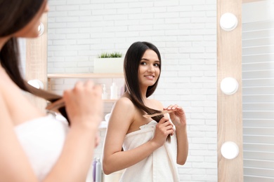 Beautiful young woman with hair brush looking into mirror in bathroom