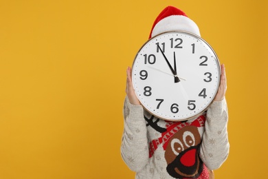 Woman with clock on yellow background, space for text. New Year countdown