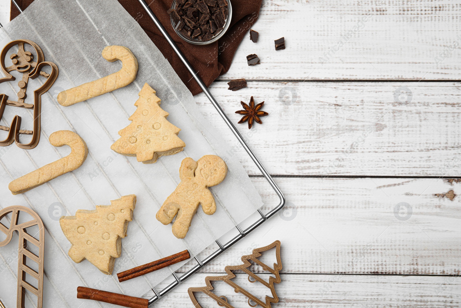Photo of Christmas treat. Flat lay composition with cookie cutters and baked biscuits on white wooden table, space for text