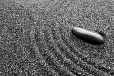 Photo of Zen garden stone on black sand with pattern, closeup