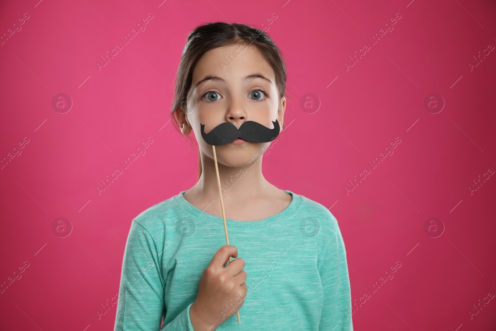 Photo of Cute little girl with fake mustache on pink background