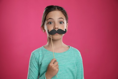 Cute little girl with fake mustache on pink background