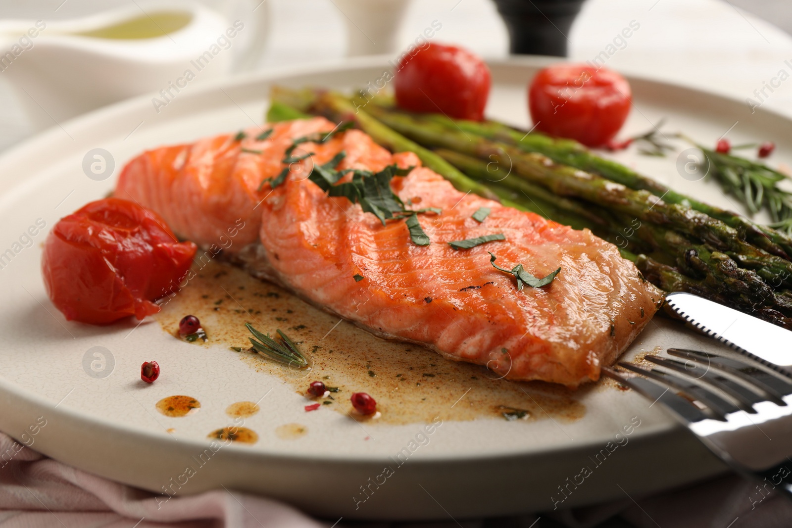 Photo of Tasty grilled salmon with tomatoes, asparagus and spices served on table, closeup